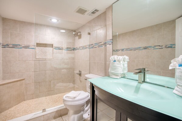 Une salle de bain avec un lavabo en verre, un miroir, une douche et des toilettes.