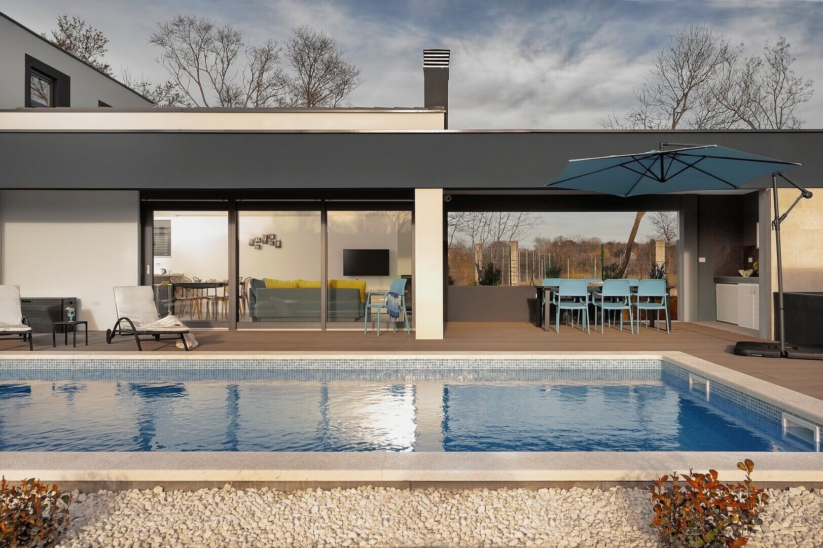 Een modern huis met een zwembad, buitenzitplaatsen en een groot raam met uitzicht op de tuin.