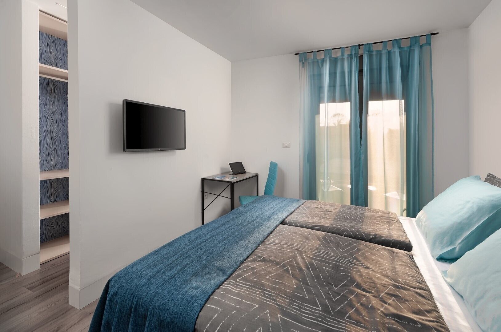 A modern bedroom with a bed, a desk, a chair, and a TV.