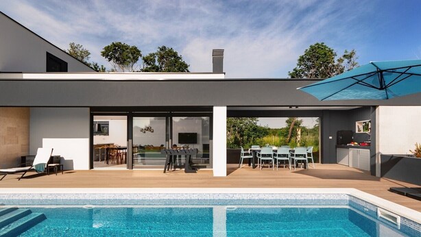 A modern house with a swimming pool, a dining area, and a kitchen visible through glass doors. - Beautiful Villa Linea near the sea with private pool! (Fazana)