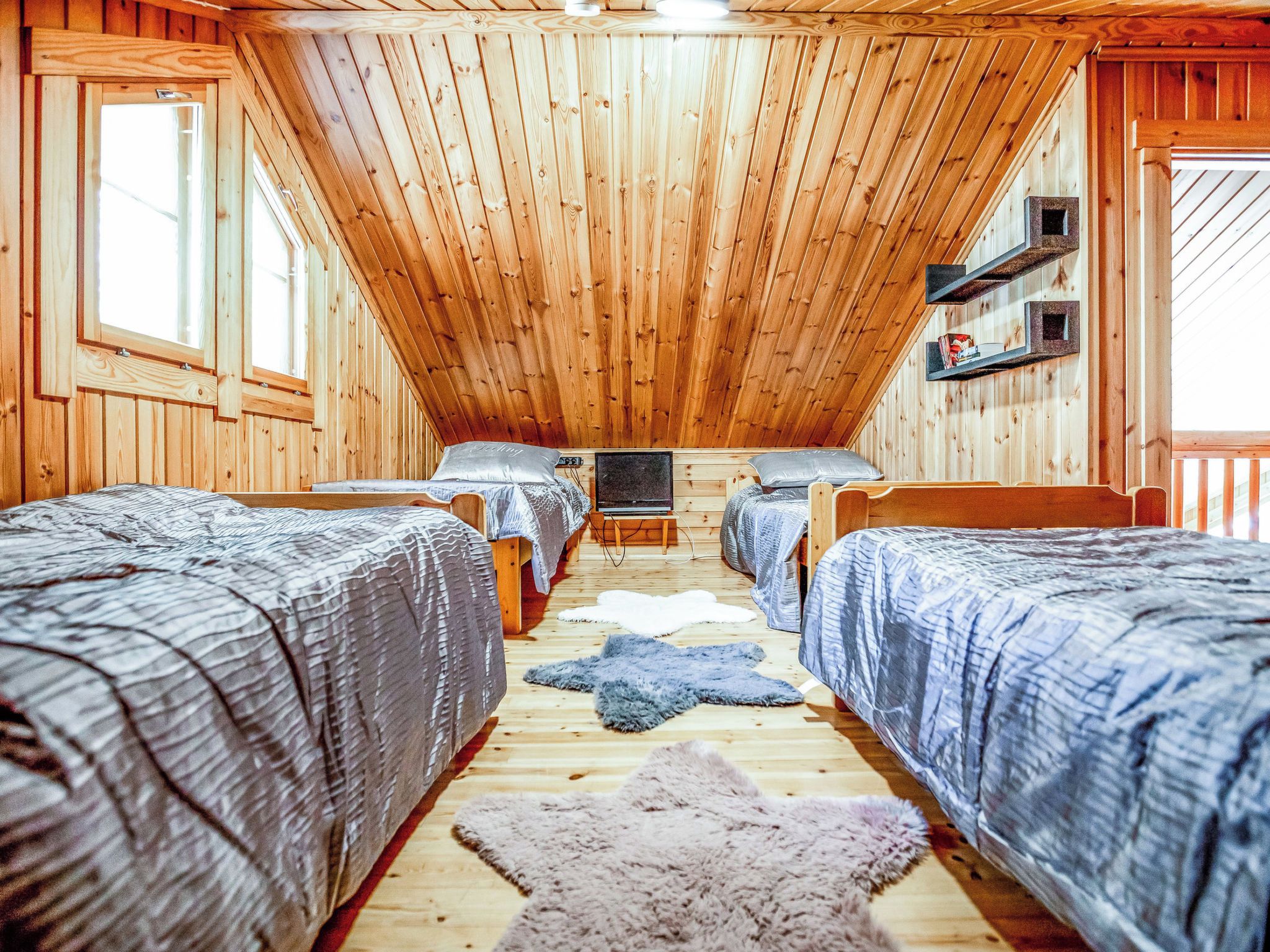 Une cabine avec trois lits en bois alignés le long d’un couloir central, un plafond avec des poutres en bois et une fenêtre sur le côté gauche.