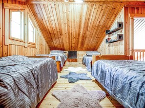 Eine Holzhütte mit drei entlang eines zentralen Ganges angeordneten Holzbetten, einer Decke mit Holzbalken und einem Fenster links.