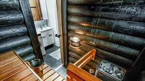 Una mesa y banco de madera en el interior de una cabaña de troncos, con chimenea y un baño pequeño y blanco.
