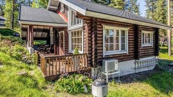 A log cabin with a porch, a small deck, and a window with a view of the surrounding forest.