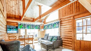 Interior de una cabaña de madera con un sofá, sillas, un televisor y un comedor.