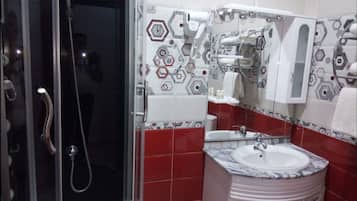 Un baño con ducha de vidrio, lavamanos con encimera de mármol y espejo encima. Las paredes están cubiertas de azulejos con un diseño geométrico.