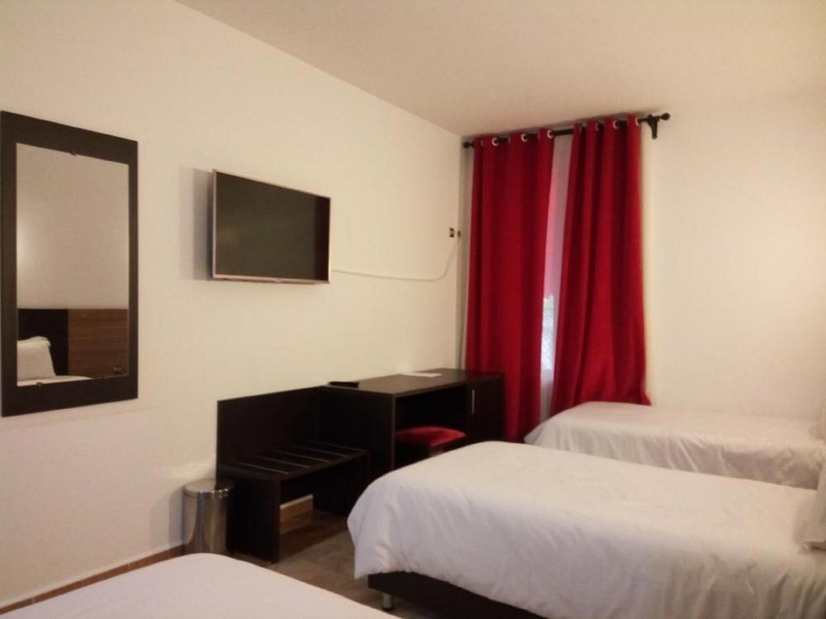 Habitación de hotel con dos camas, televisión, escritorio y cortinas rojas.