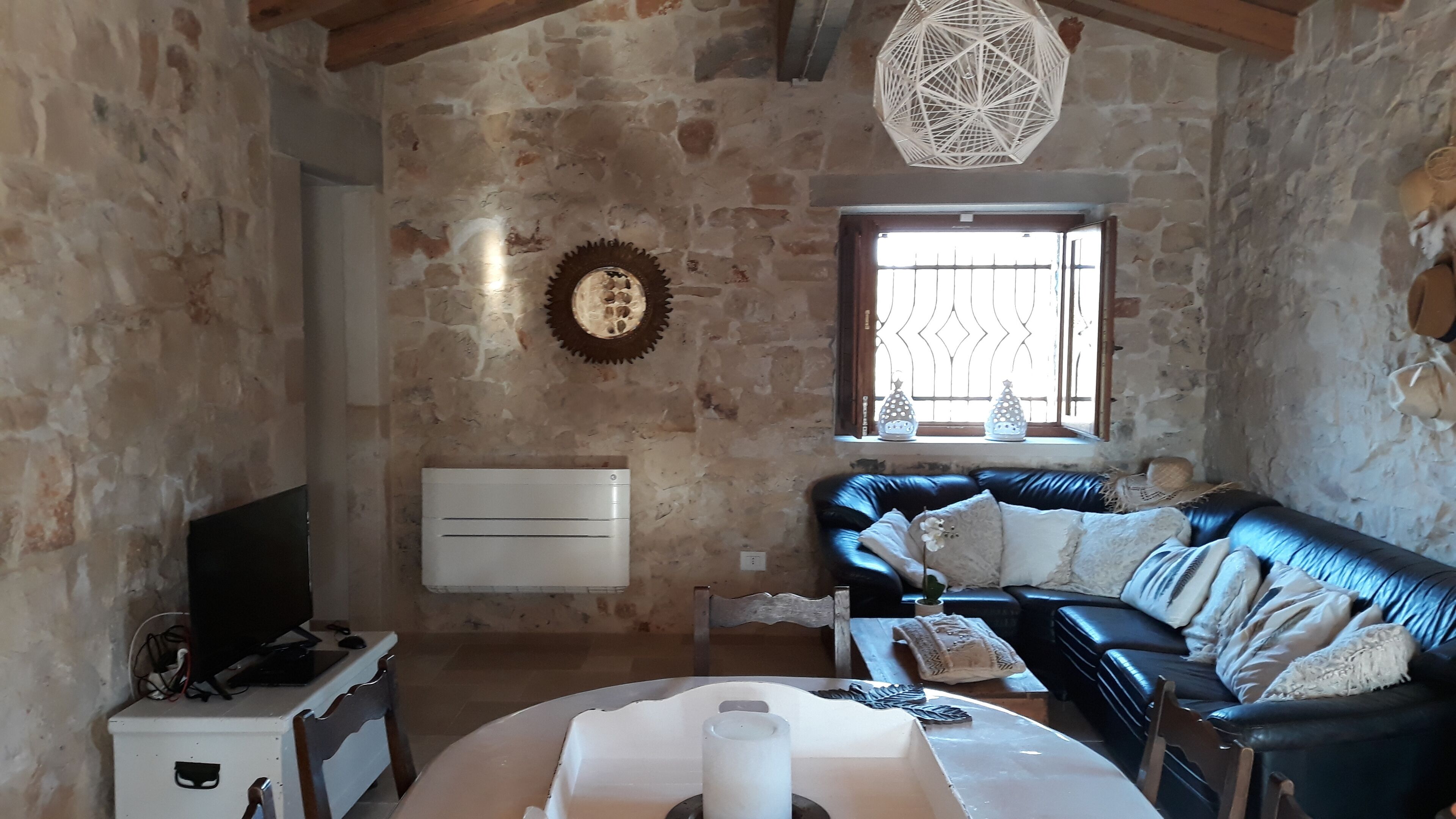 Une pièce au style rustique, avec des murs en pierre, un canapé en cuir noir, un bureau blanc avec un ordinateur et une grande fenêtre ornée de vitraux.