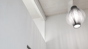 Ein modernes Interieur mit weißer Decke, einer außergewöhnlichen, strukturierten Leuchte und einer minimalistischen Fischskulptur an der Wand.