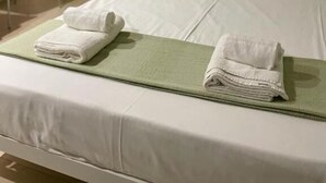 Ein ordentlich bezogenes Bett mit weißen Leinen und zwei gefalteten Handtüchern auf einer grünen Unterlage.