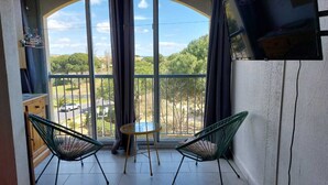 A balcony with two green chairs, a small round table, and a TV on the wall. - Sea view, beach and port 2m away on foot, private parking  (Agde)