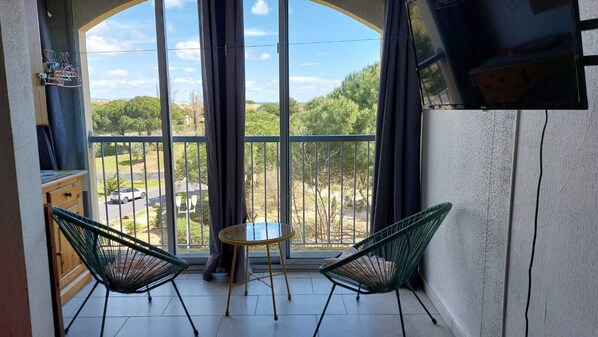 A balcony with two green chairs, a small round table, and a TV on the wall.