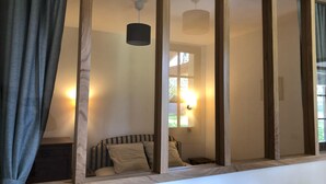 A room with a bed, a nightstand, a lamp, and a window with curtains. - In a green setting, pretty farm (producing walnuts and strawberries), swimming pool (Cendrieux)
