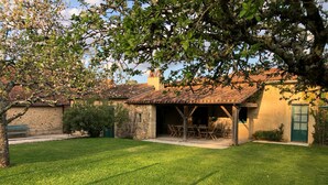 A rustic stone building with a tiled roof, a covered patio with wooden furniture, and a well-maintained lawn. - In a green setting, pretty farm (producing walnuts and strawberries), swimming pool (Cendrieux)
