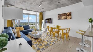 A modern living room with a sofa, coffee table, and a dining area with yellow chairs. - Midtown Miami 1BR · Free Parking + Wynwood Nearby (Miami)