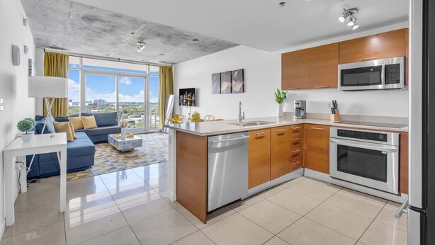 A modern kitchen with stainless steel appliances, wooden cabinets, and a large window offering a city view. - Midtown Miami 1BR · Free Parking + Wynwood Nearby (Miami)