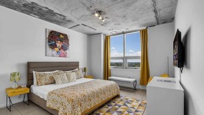 A modern hotel room with a large bed, a window with curtains, a flat-screen TV, and a ceiling with exposed beams. - Midtown Miami 1BR · Free Parking + Wynwood Nearby (Miami)