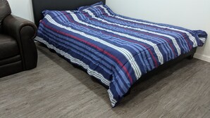 Un lit simple avec une couvre-lit à rayures, dans une chambre dont la tête de lit est de couleur sombre et qui contient un fauteuil en cuir marron.