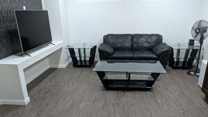 Un salon moderne avec un canapé en cuir noir, une table basse en verre et un téléviseur posé sur un meuble blanc.