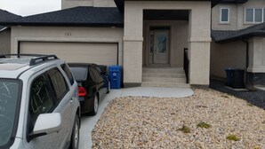 Une maison d’habitation avec un garage, des voitures garées et une allée gravillonnée.