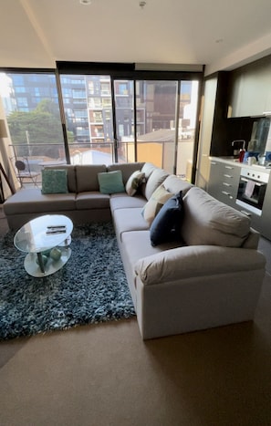 A modern living room with a sectional sofa, a glass coffee table, and a view of a cityscape through large windows. - Modern Luxurious with private parking & free Wi Fi (South Yarra)