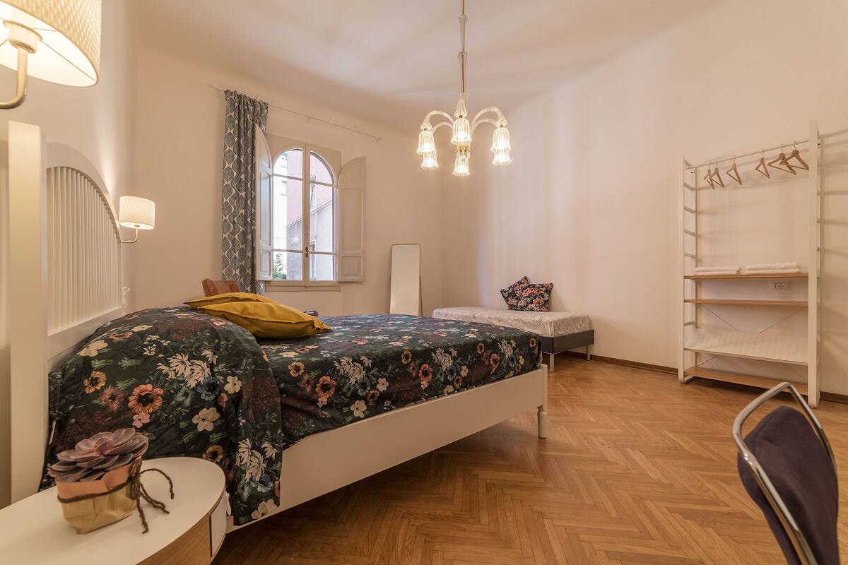 A bedroom with a bed, bedside table, lamp, wardrobe, and a window with curtains.