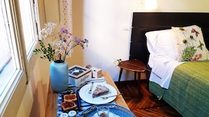 A neatly arranged breakfast table with a vase of flowers, a plate of toast with jam, a slice of cake, and a small glass of tea. - Tilia (Bologna)