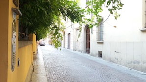 A cobblestone street flanked by buildings with arched doorways and a yellow wall on the left. - Tilia (Bologna)