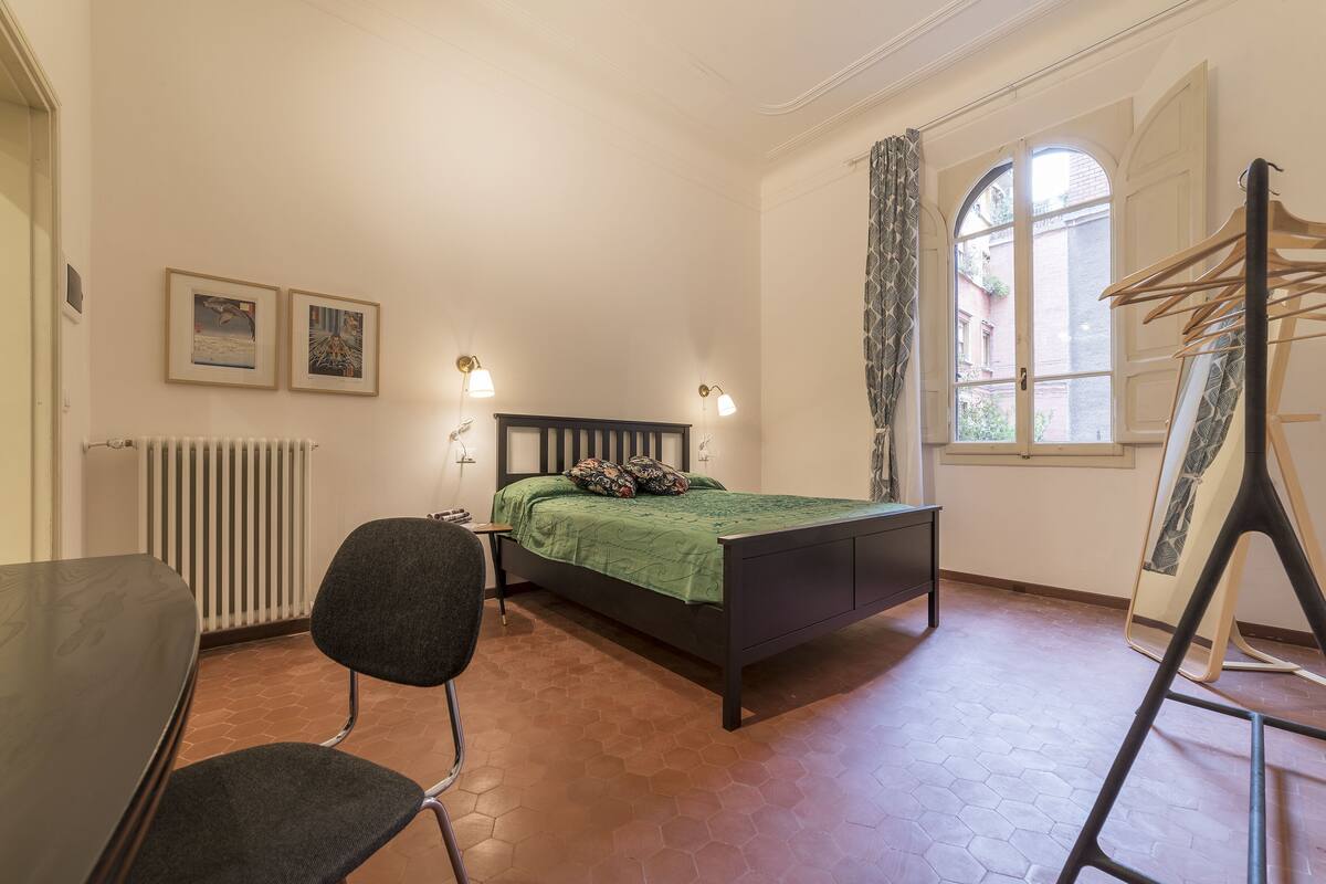 A bedroom with a bed, a chair, a radiator, and a window with curtains.