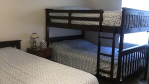 Quarto com duas camas beliche, um ventilador de teto, uma mesa de cabeceira e uma janela.