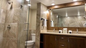 A modern bathroom with a glass-enclosed shower, a large mirror, and a vanity with a sink and towel dispensers. - Peaks Penthouse #643 (Mountain Village)
