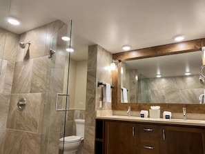 Een moderne badkamer met een douchecabine van glas, een grote spiegel en een wastafelmeubel met een wastafel en handdoekdispensers.