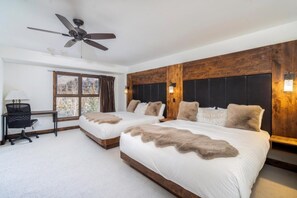 A hotel room with two beds, a desk, a chair, a ceiling fan, and a window with curtains.