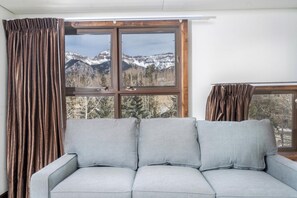 Een kamer met een grijze bank die uitkijkt op een bergzicht.