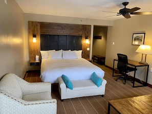 Een hotelkamer met een groot bed, een bureau, een stoel en een plafondventilator.