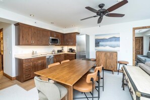 A modern kitchen with wooden cabinets, a stainless steel refrigerator, and a dining area with a wooden table and chairs.