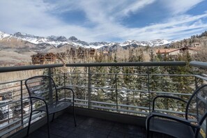 Un balcon doté de rampes en métal, offrant une vue sur un paysage montagneux avec des sommets enneigés et des bâtiments.