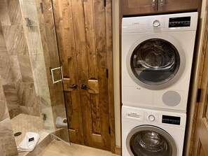 Een badkamer met een houten deur, een douche en twee Bosch wasmachines boven elkaar.