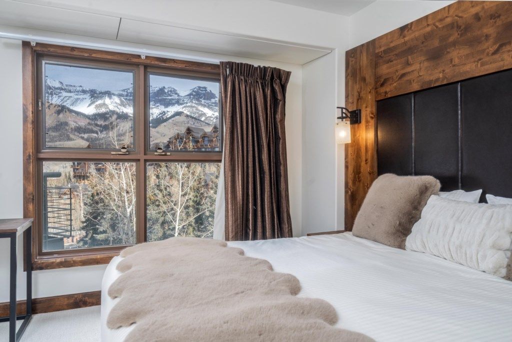A bedroom with a large window, a bed with white bedding, and a wooden headboard.