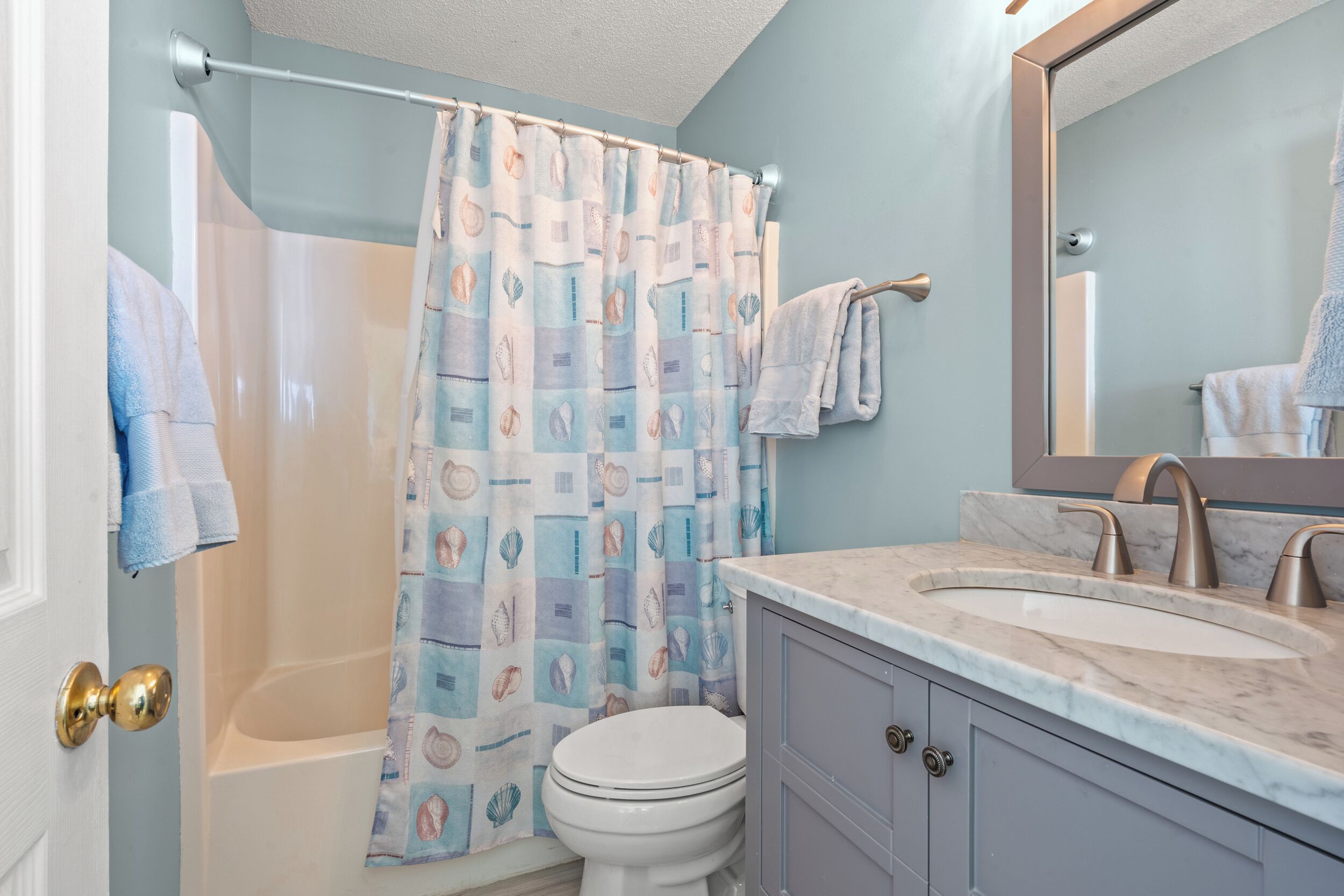 A bathroom with a shower curtain, two sinks, a toilet, and a mirror.