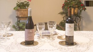 Una mesa de comedor dispuesta con botellas de vino y copas, rodeada de adornos en la pared y plantas en macetas.