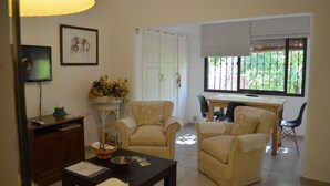 Una sala de estar con un sofá, sillones, una mesa de centro, un televisor y un comedor con mesa y sillas.