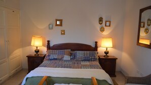 Una cama bien hecha con ropa de cama escocesa, dos lámparas de noche y un espejo en la pared.