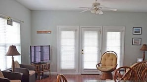 Ein Wohnzimmer mit Glastisch, Korbstühlen, einer Couch und einem Deckenventilator.