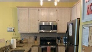 A kitchen with light wood cabinets, stainless steel appliances, a granite countertop, and a black rug.