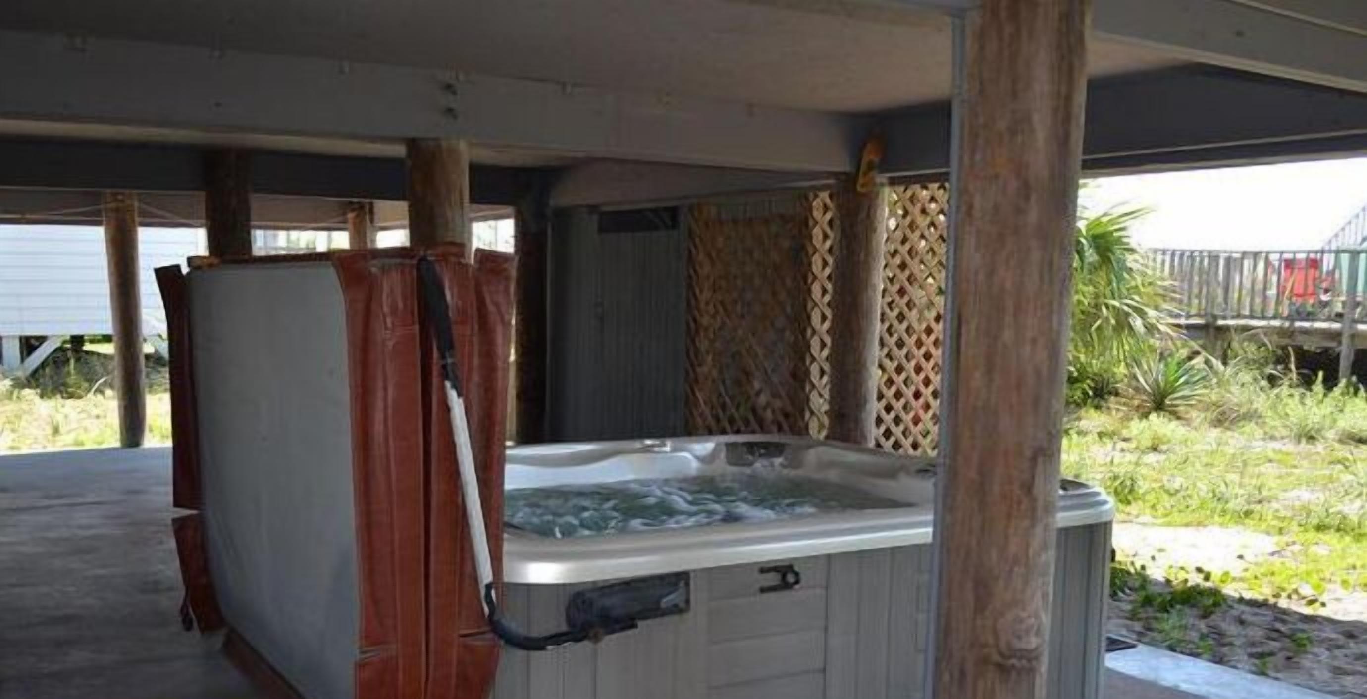 A hot tub under a covered area with wooden pillars and a lattice fence in the background.