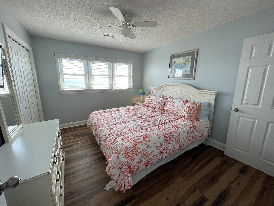 A bedroom with a bed, a ceiling fan, a window, and a door.