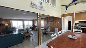 Uma sala de estar ampla com uma mesa de jantar de madeira, cadeiras brancas e um sofá azul.