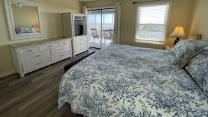 Um quarto com cama, cômoda, televisão e varanda com vista.
