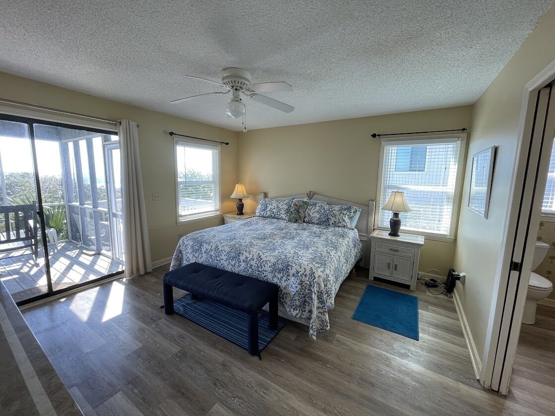 A bedroom with a bed, a bench, a nightstand, a ceiling fan, and a view of the outdoors.